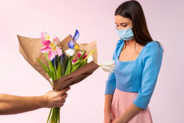 Tıbbi maskeli esmer bir kadın. Kafası, tembel lalelerin doğumundan dolayı eğik. Pembe neon arkaplan.