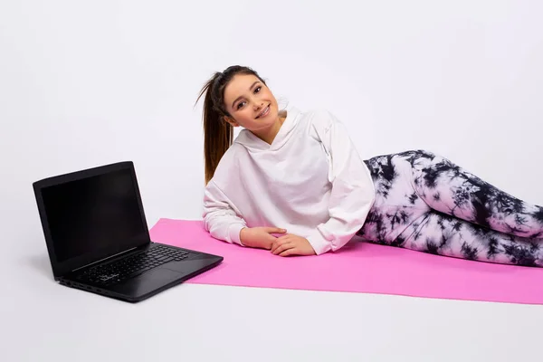 Yoga lessons online. Positive yoga girl doing morning practice in front of laptop at home, white background