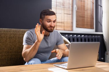 Genç adam çevrimiçi iletişim. Video konferans uygulaması ile akrabalarıyla ya da arkadaşlarıyla görüntülü konuşma yapıyor. Aile toplantısı var. Uzak iletişim interneti, ekranı izlemek için el salla