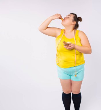 Güzel boyut artı model, diyet konsepti boynunda taksimetre, elinde kek kasesi. Şişman kadın tatlı kremalı keklerin tadını çıkarıyor..