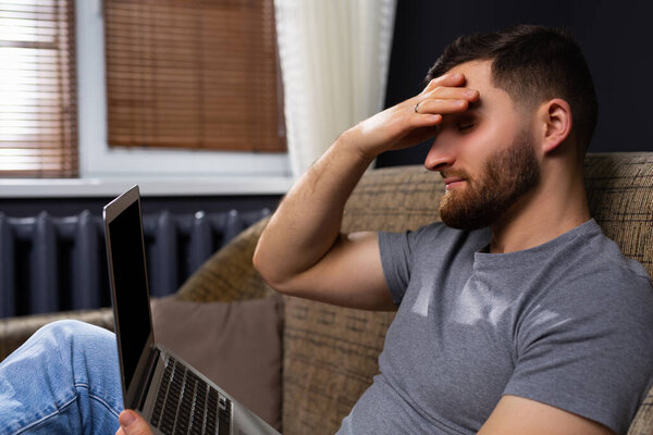 Профиль фотографии уставшего кавказского бизнесмена, сидящего дома на диване с ноутбуком. Работа из дома онлайн.