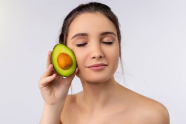 Kafkasyalı hoş bir kadın, elinde avokado, spa, güzellik ve diyet konseptiyle gözlerini kapatıyor.