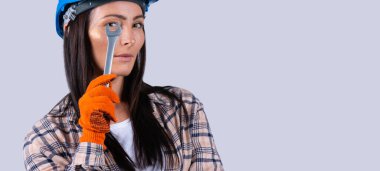 Banner, uzun format. Kafkas portresi, kasklı gülümseyen güzel bir bayanın gri fotokopi arkaplanındaki ingiliz anahtarı aletlerinden kameraya bakması..