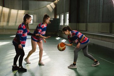 Lisedeki kadın basketbol takımı oyunu oynuyor. Spor üniformalı bir grup mutlu genç kız içeride basketbol oynuyorlar.