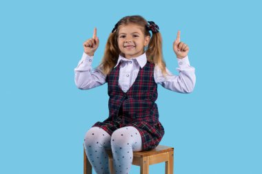 Yakından profil portresi. Güzel, çekici, neşeli, mutlu, düz saçlı, iki parmağıyla kameraya bakan sarışın kız. Mavi arka planda izole edilmiş.