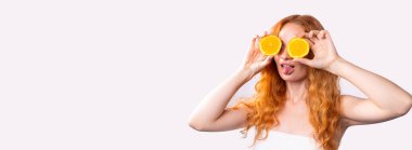 Banner, uzun format. Kıvırcık kızıl saçlı bir kız, banyo havlusuna sarılmış ve gözleri yerine portakal dilimlerini tutan korsaj doğumları yapıyor. Reklam için boş alan.