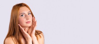 Kızıl kadın, cilt bakımı ve güzellik konsepti. Neşeli, gülümseyen, temiz tenli, bakımlı vücutlu, gri arka planda çıplak, bilgi için boş bir yan alanı olan kızıl saçlı kız.