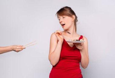 Genç bir sarışın ahşap yemek çubuklarını reddediyor ve yemek için çatalı tercih ediyor. Kız çatalla suşi yiyor. Gri stüdyo geçmişi.