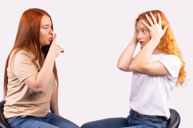 Genç kızıl saçlı kız sessiz jest yapıyor, sessiz ol, sessiz ol, korkmuş arkadaşına sessiz ol diyor, sessiz ol diyor. Sessizlik ya da gizli, gri arkaplan, bedava uzay metni. Yüksek kalite fotoğraf