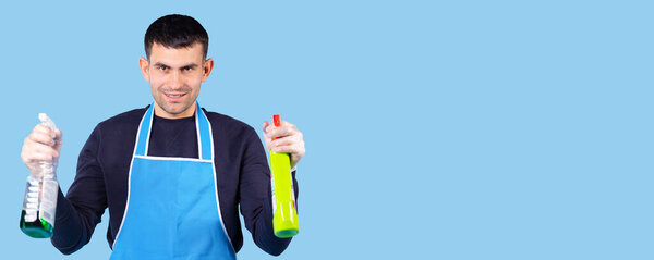 Banner, long format. Young man in uniform and in protective gloves posing holding two cleaners for cleaning the house. Empty side space.