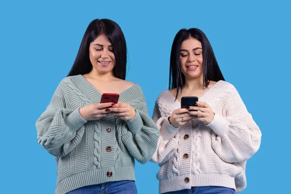 Two Beautiful Girls Twins Smiling Looking Smartphone Blue Background High — Stock Photo, Image