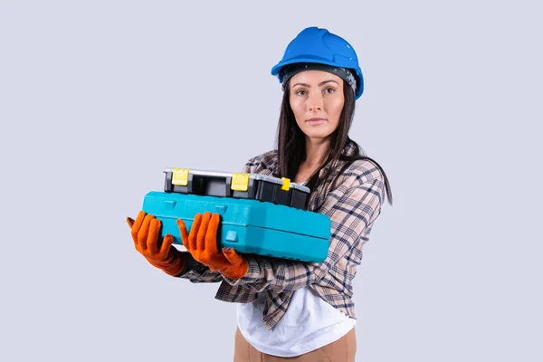 Vit kvinna tittar allvarligt på kameran håller verktygslåda i verkstad isolerad grå bakgrund. Kvinnlig ingenjör och industrikoncept — Stockfoto