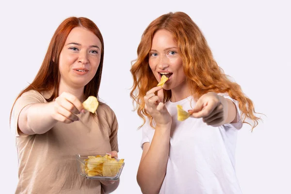 Close up de dois gengibre, meninas de cabelos vermelhos do sexo feminino, amigos segurando tigela com batatas fritas frescas compartilhando com os amigos na festa em casa. Mostrando chips de lanche para câmera, sorrindo — Fotografia de Stock