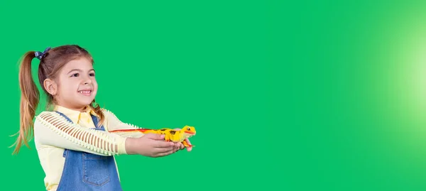 Bannière, format long. Une écolière montre un jouet, lézard. Souriant et gardant le jouet dans ses mains. Fond vert. — Photo