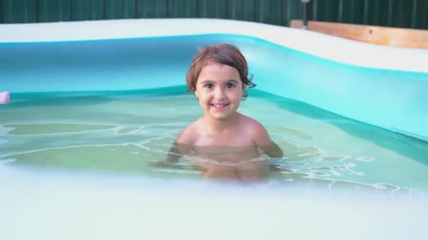 Niña feliz divirtiéndose dentro de una piscina al aire libre en verano, saludando de la mano y ella está complacida. — Vídeos de Stock