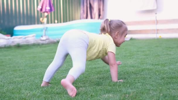 Nettes blondes Mädchen, das draußen auf dem grünen Gras herumalbert wie eine kleine Spinne am Swimmingpool. — Stockvideo