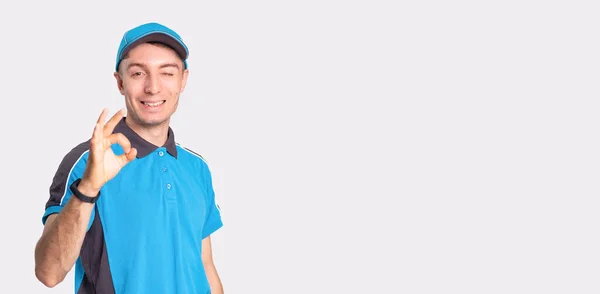 Foto de um homem de entrega sorridente em pé na frente da câmera mostrando com o gesto tudo está bem e piscando. — Fotografia de Stock