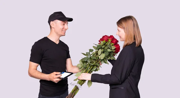 Bizneswoman dostała bukiet kwiatów od kuriera w czarnym mundurze i musi podpisać odbiór przesyłki.. — Zdjęcie stockowe