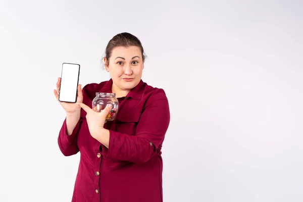 En vacker överviktig kvinna visar sin mobiltelefon håller i den andra handen en burk färgglada sötsaker. — Stockfoto
