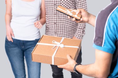 Kurye teslimat yaparken akıllı telefonu tutuyor ve hediye beyaz kurdeleyle bağlanmış bir paketin fotoğrafını çekiyor..