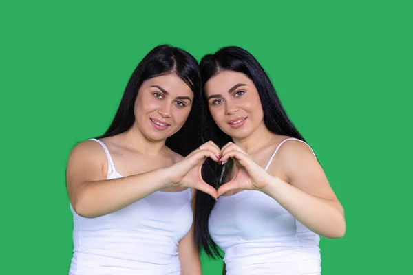 Duas meninas bonitas em t-shirt branca com tiras encostadas uma contra a outra e colocar as mãos juntas e fez sinal de coração — Fotografia de Stock