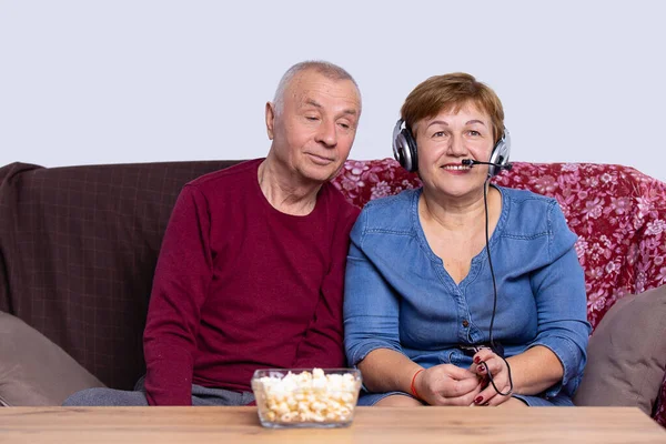 Retirement couple are sitting together on a couch, woman wearing headphones speaking into the microphone. — Φωτογραφία Αρχείου