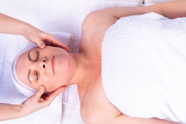 Spa salonunda masaj masasında uzanan güzel, rahatlatıcı bir kadına yüz masajı yapan bir uzman..