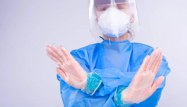 머리에 고정 된 의료 제복을 입고 마스크를 쓰고 보호 창문을 착용하고 수술을 하는 여성 이 바이러스가 멈추는 신호로 양손을 가로질렀다.. — 스톡 사진