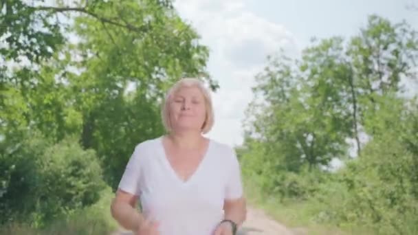 Primer plano de vídeo de la mujer feliz corriendo a lo largo del camino del bosque mirando a la cámara de vídeo con la cara sonriente. — Vídeos de Stock