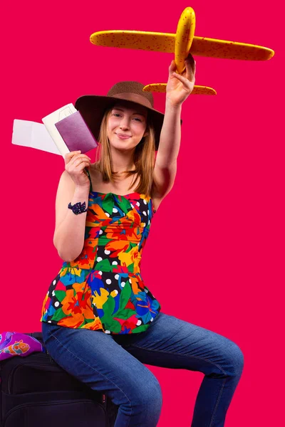 Femme blonde portant une blouse multicolore avec un jean et assise sur sa valise avec passeport vaccinal et billets prêts à voler. — Photo