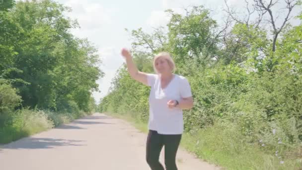 Sportliche Fitness-Frau läuft mit dem Gesicht zur Kamera zurück und ruft nach jemandem, der mit den Händen winkt. — Stockvideo