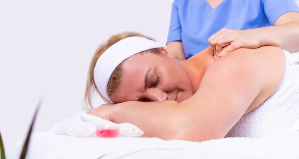 Specialist maken schouder massage aan een volwassen vrouw ontspannen en liggen met gesloten ogen in een schoonheidssalon . — Stockfoto