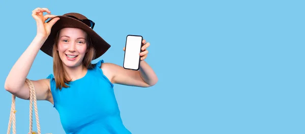 Mujer joven agradable en un sombrero y con una blusa azul sosteniendo el teléfono inteligente y se mantiene en el borde del sombrero. — Foto de Stock