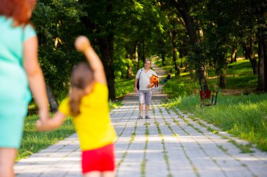 Baba günü geldi, anne ve küçük kızı uzaklarda ona bakıyorlar, küçük kız ona el sallıyor ve babası güzel kızı için bir oyuncak ve çantayla ayakta duruyor..