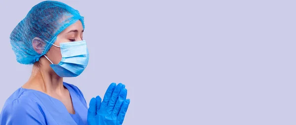 La doctora en uniforme médico azul y máscara con los ojos cerrados está rezando por una rápida recuperación de la gente. — Foto de Stock