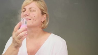 Sivilceli sarışın bir kadın odada oturup yüzünü kozmetik buharla temizliyor ve kendini daha iyi hissediyor..