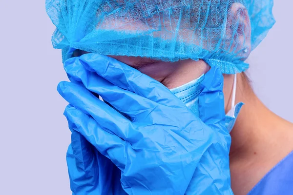 Sjuksköterskan i medicinsk uniform, mask och handskar stängde ansiktet med händerna eftersom hon är trött. — Stockfoto