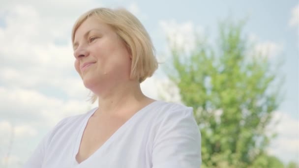 Glückliche blonde Frau mittleren Alters genießen das Leben erhob die Hände nach oben und breitete die Arme seitlich in die Sonne und dann in die Videokamera. — Stockvideo