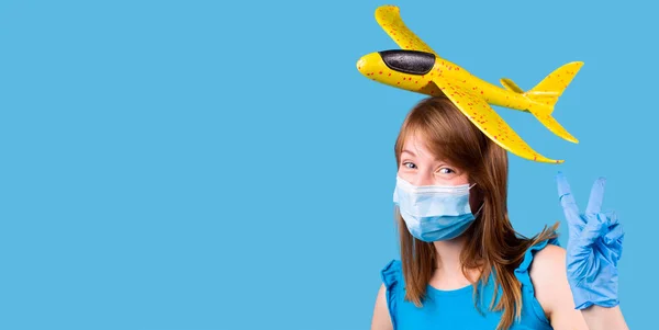 Позиція радісної дівчини в медичних рукавичках і масці з іграшковим літаком на голові жовтого кольору . — стокове фото