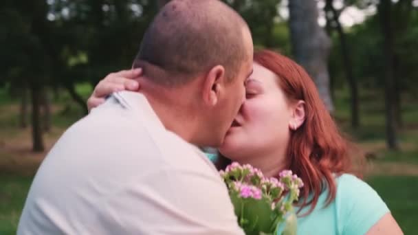 Ganska gifta par tillbringar tid på en dejt i parken kramas och kysser varandra hålla blomman i händerna. — Stockvideo