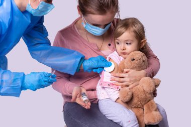 Salgın sırasında, tıbbi maske takan anne küçük kızıyla birlikte küçük kız aşısını yapmak için doktora geldi..