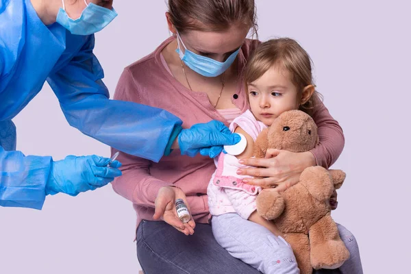 En el tiempo pandémico la madre en la máscara facial médica ha llegado con su hija pequeña al médico poner la vacuna de niña. — Foto de Stock