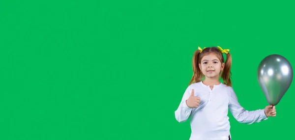 Καλό κορίτσι κρατά το λαμπρό πράσινο μπαλόνι στο χέρι της και κάνει χειρονομία με τον αντίχειρα προς τα πάνω λέγοντας ότι είναι εντάξει. — Φωτογραφία Αρχείου