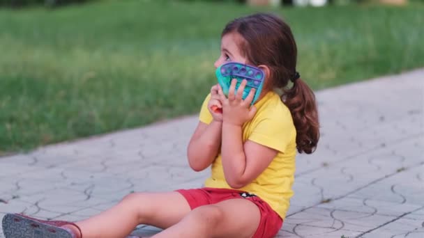 Krásná dívka sedí na pěší stezce v parku drží v náručí mraveniště stresu hračka barevné pop to, ona miluje to moc a objímá ji na hrudi. — Stock video