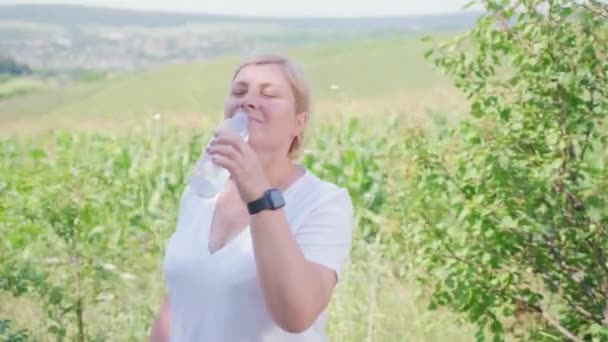 Γυναίκα n μεσήλικας φορώντας ψηφιακή μάγισσα κρατώντας ένα μπουκάλι νερό και πίνει στέκεται ανάπαυση και απολαμβάνοντας τη φύση. — Αρχείο Βίντεο