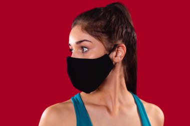 Close up photo of a nice young girl wearing the textile mask of black color turned her head to the right side.