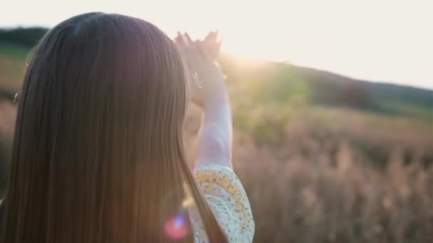 Hermosa joven con el pelo largo en el campo extendiendo sus manos hacia adelante con manicura rosa y cruzó las palmas para cerrar el sol. — Vídeos de Stock