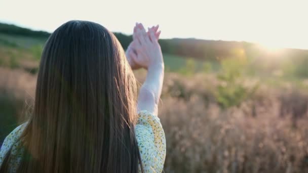 Bela jovem loira de cabelos longos usando vestido floral cruzou as palmas das mãos com os braços estendidos para a frente e desfrutando do pôr do sol no campo. — Vídeo de Stock