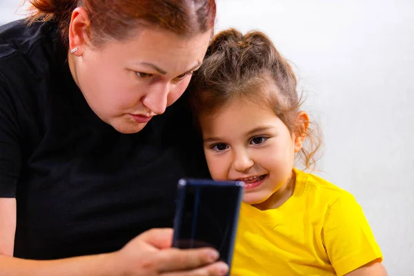 Close up foto de mamãe e menina sentados no sofá e assistindo a notícias ruins manchetes usando telefone celular, eles são viciados em telefone. — Fotografia de Stock