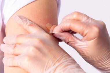 Koruyucu tıp eldivenli doktor kadın koluna pandemik aşıdan sonra bandaj yapıştırıyor..